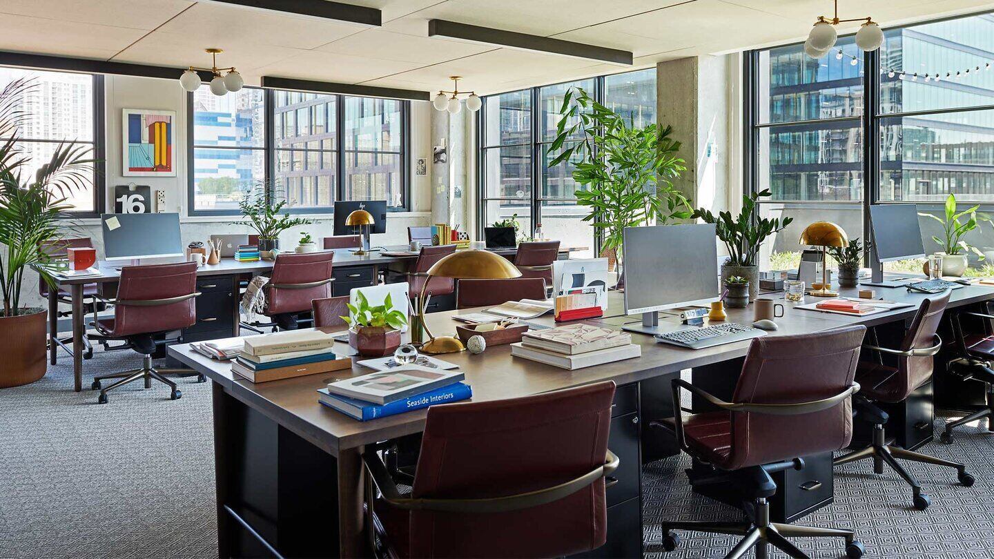 An office with 16 desks, with large windows on both visible walls. There is lots of space.