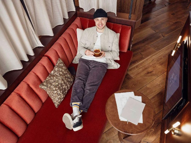 Man in beanie hat enjoying a long black coffee lounging on a day bed
